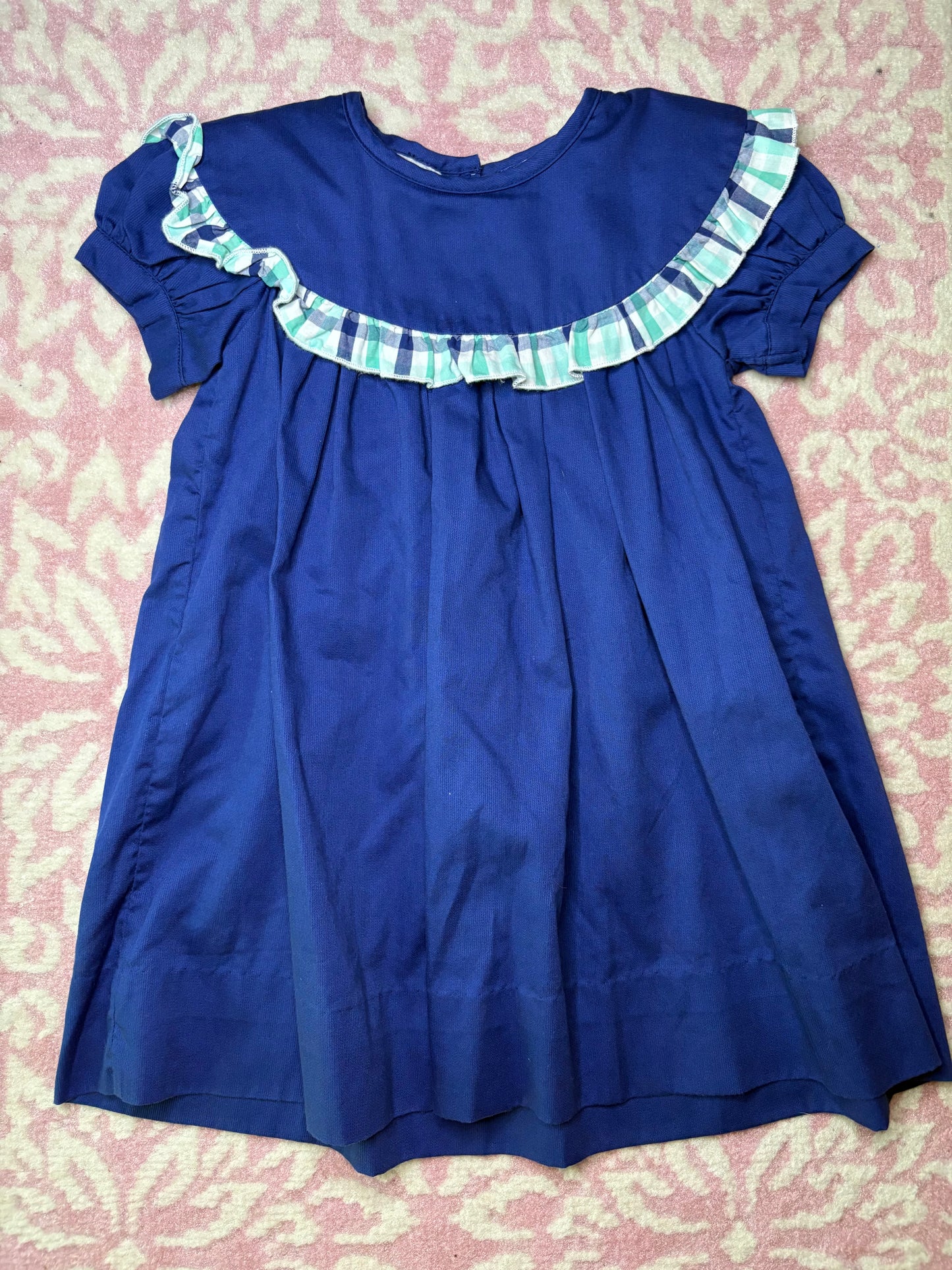 Navy blue short sleeve girls dress with plaid ruffle trim, laid on pink patterned rug
