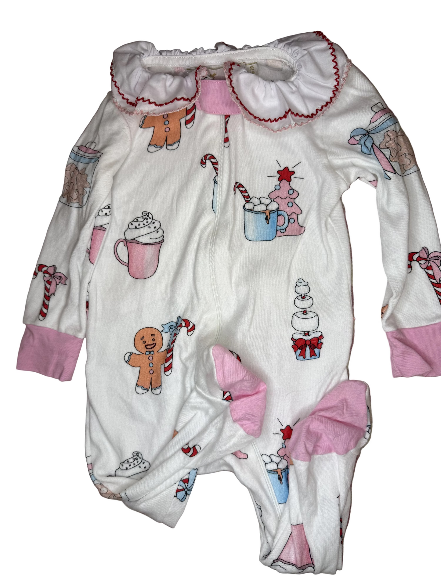 White baby footie pajamas with pink cuffs, ruffled collar, and holiday print featuring gingerbread, candy canes, hot cocoa, and gifts on a plain background.