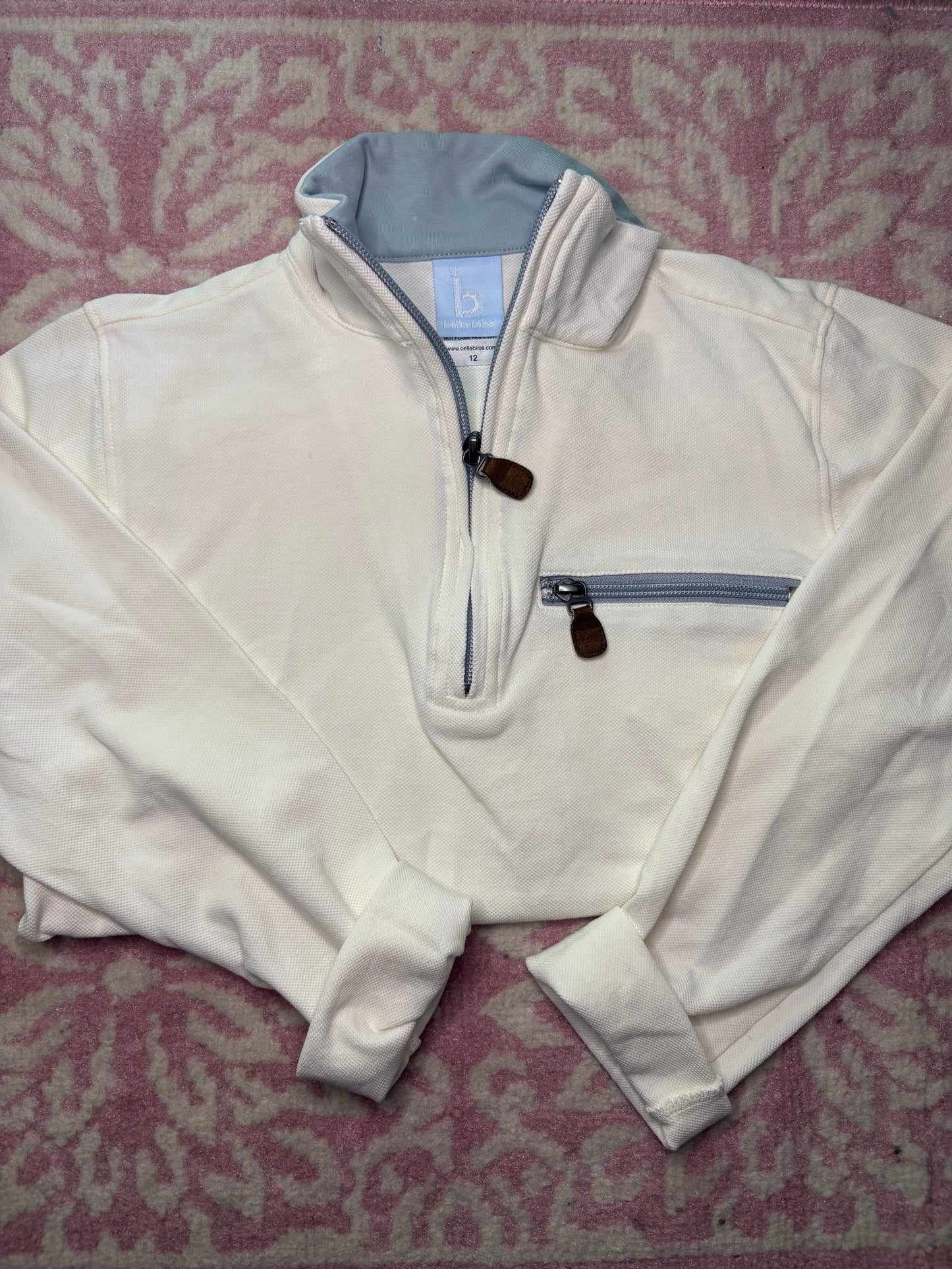 Kids cream quarter-zip pullover with gray collar and front zip pocket on pink patterned rug