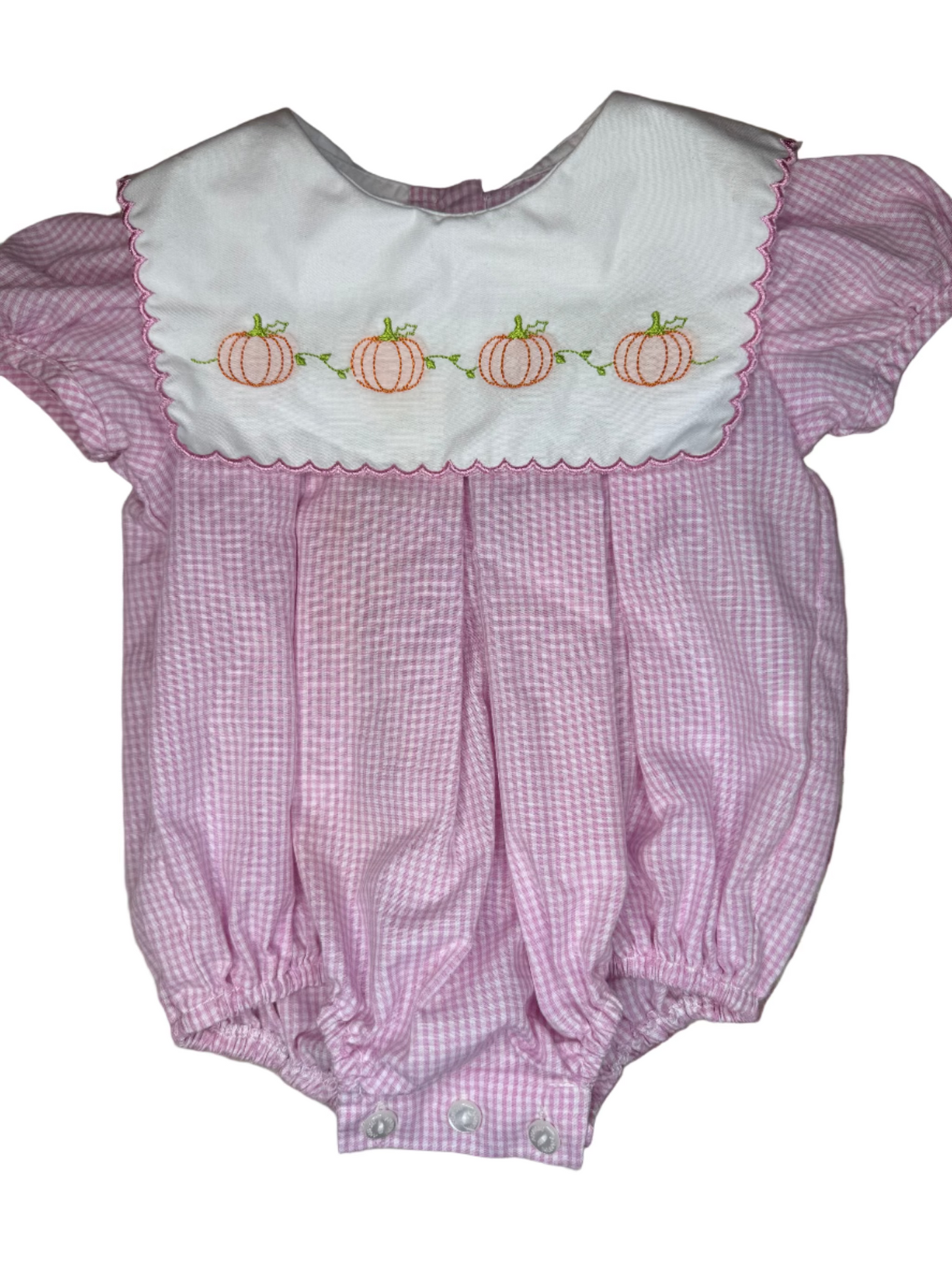 Pink checkered baby romper with white collar featuring embroidered pumpkins on a patterned surface.