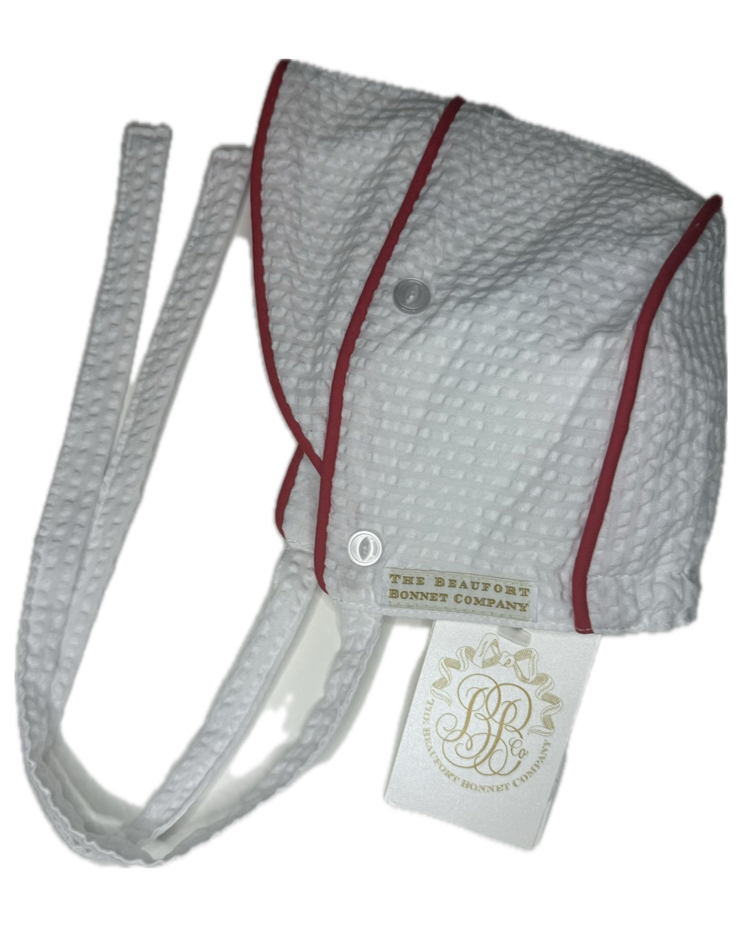 White seersucker baby bonnet with red trim and straps, tag attached, on white background