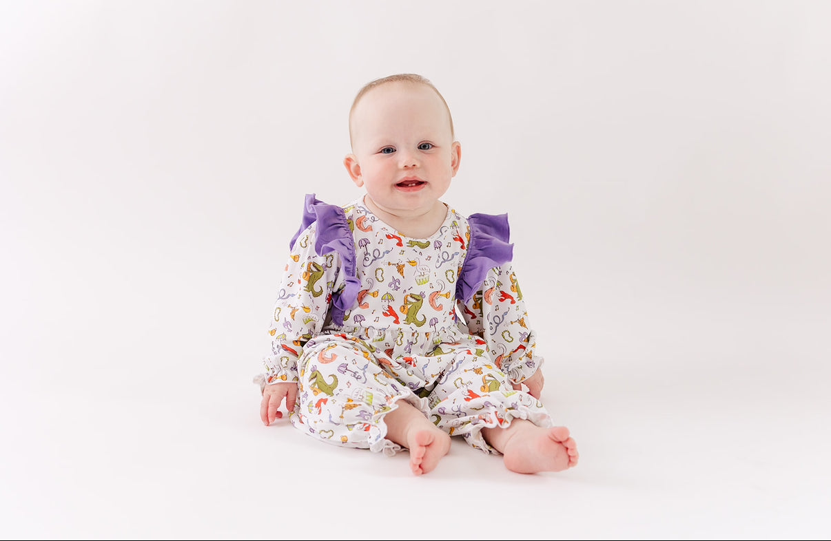Baby in animal print romper with purple ruffles on sleeves, sitting on white background
