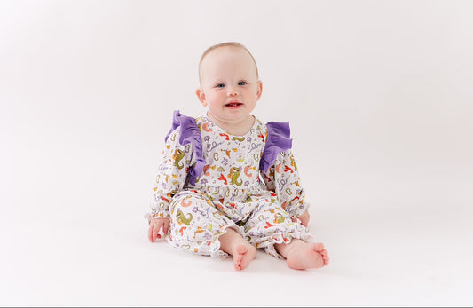 Baby in animal print romper with purple ruffles on sleeves, sitting on white background