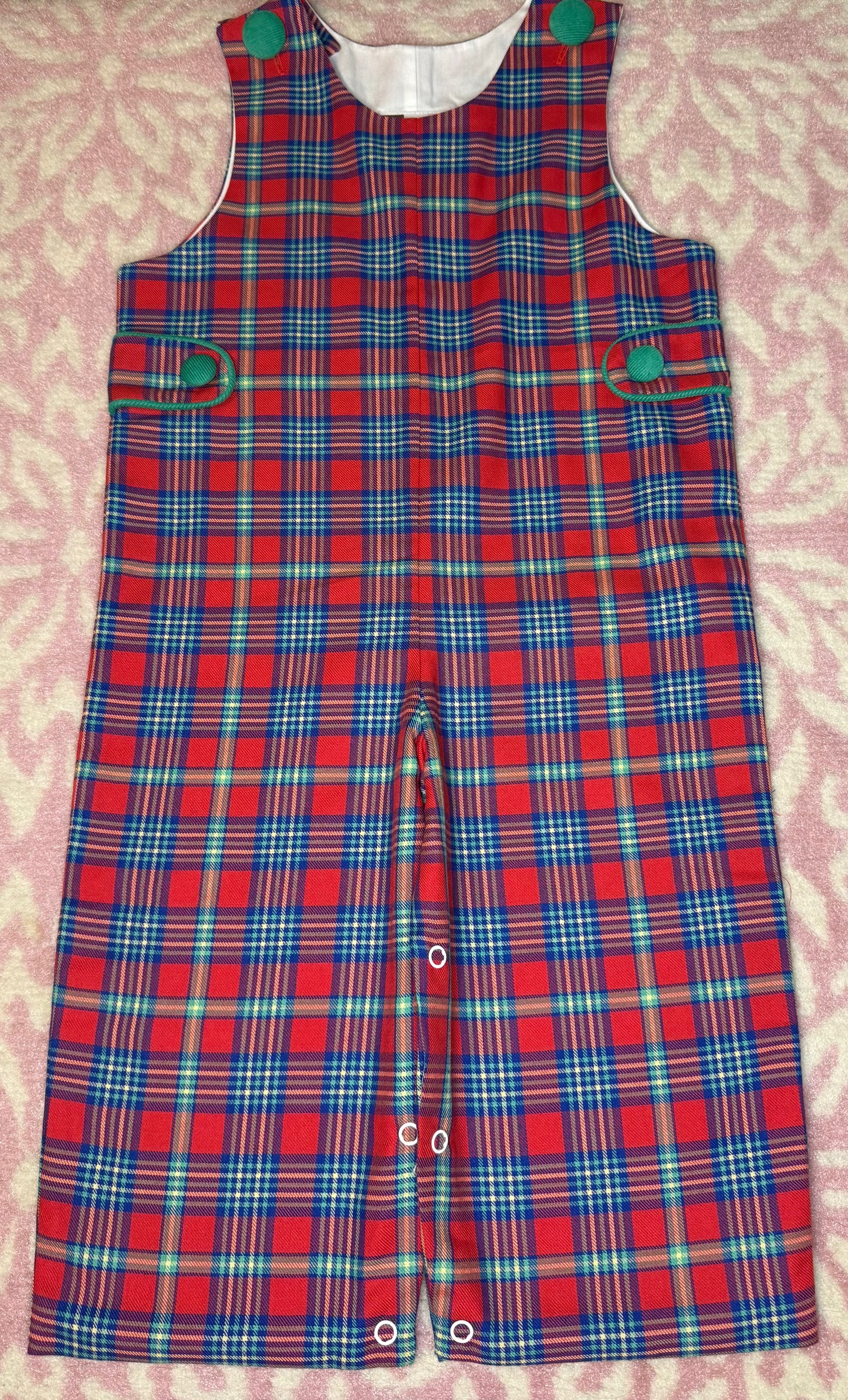 Red plaid toddler romper with green button details on pink patterned background