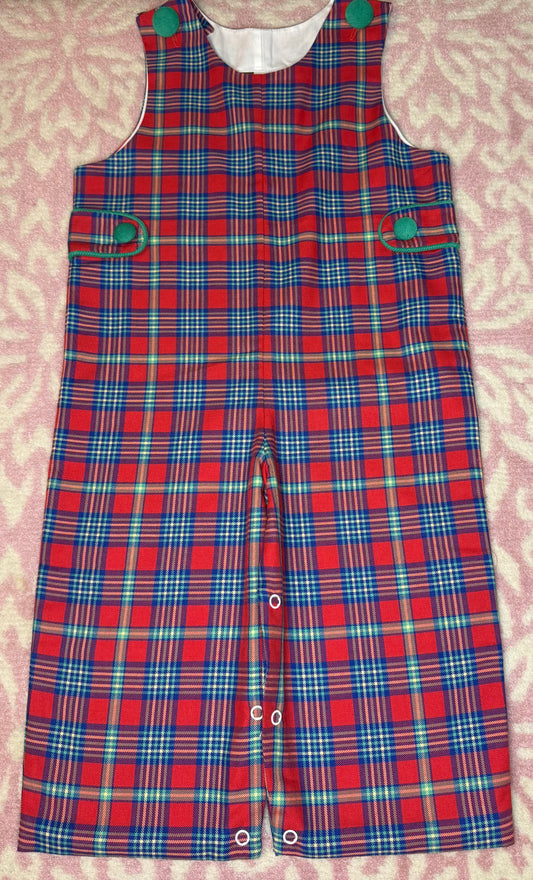 Red plaid toddler romper with green button details on pink patterned background