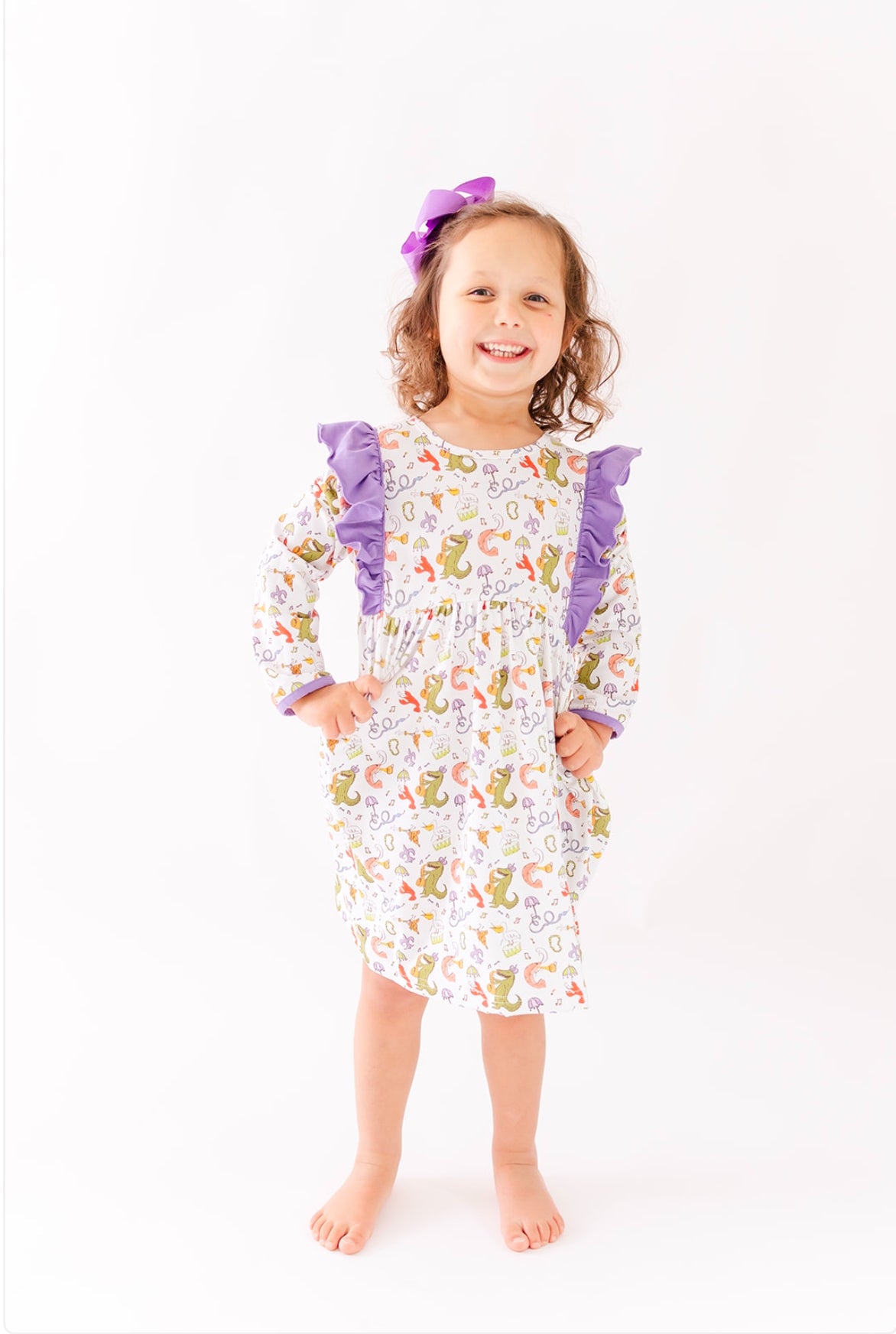 Smiling girl wearing long sleeve ruffle dress with colorful animal print and purple bow
