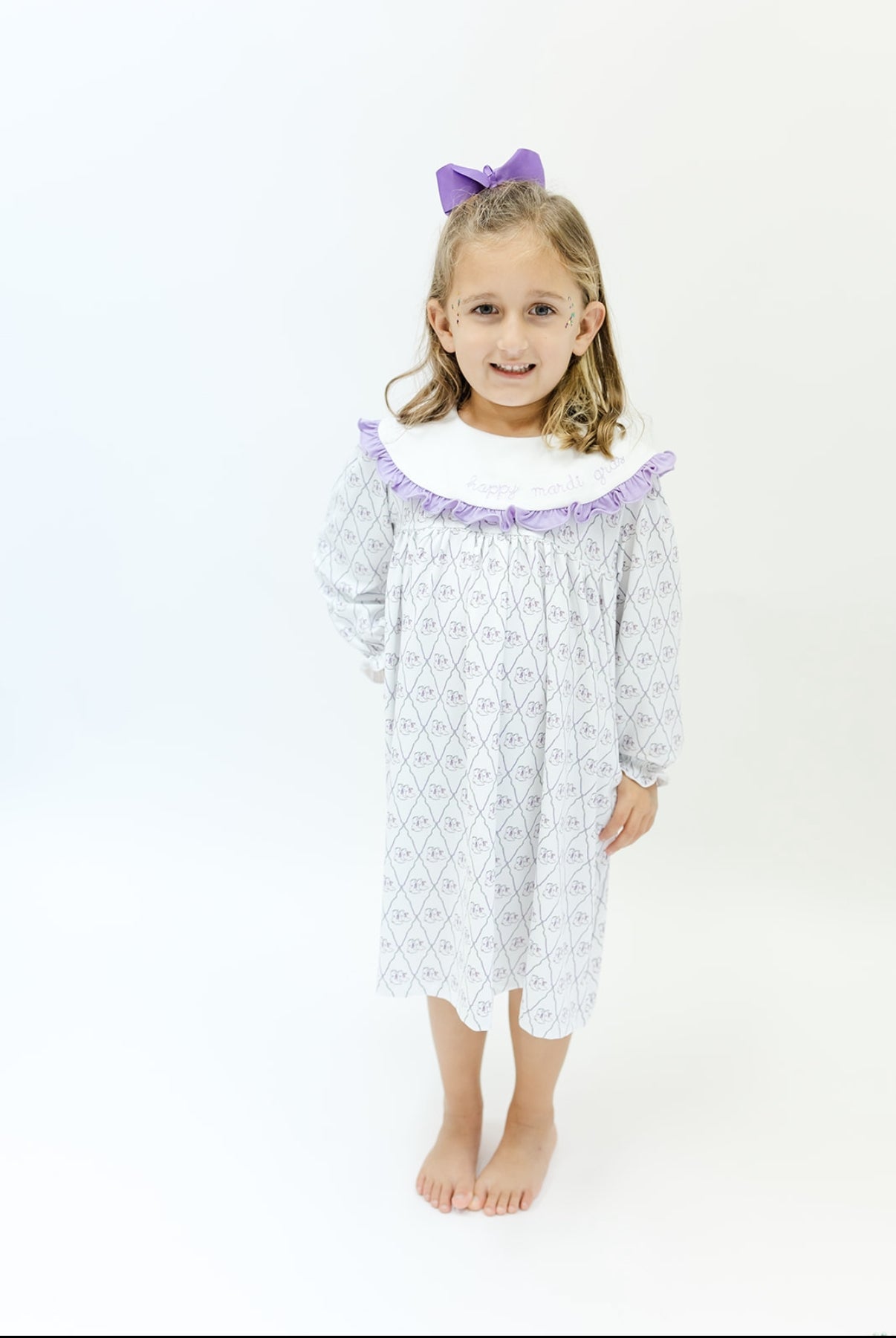 Smiling girl in a long-sleeve white nightgown with lavender trim and a purple hair bow