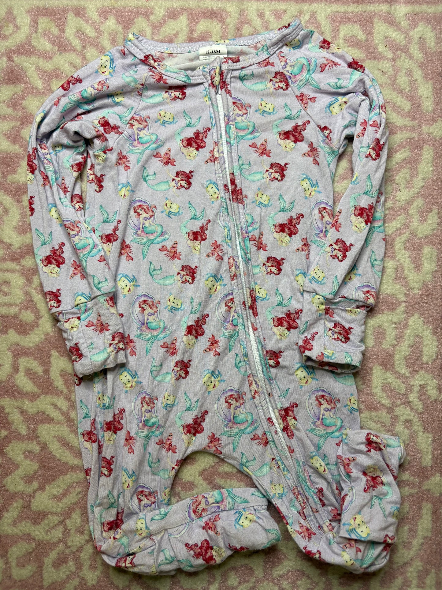 Little Mermaid themed infant footed pajama with zipper, pastel colors, laid on patterned rug