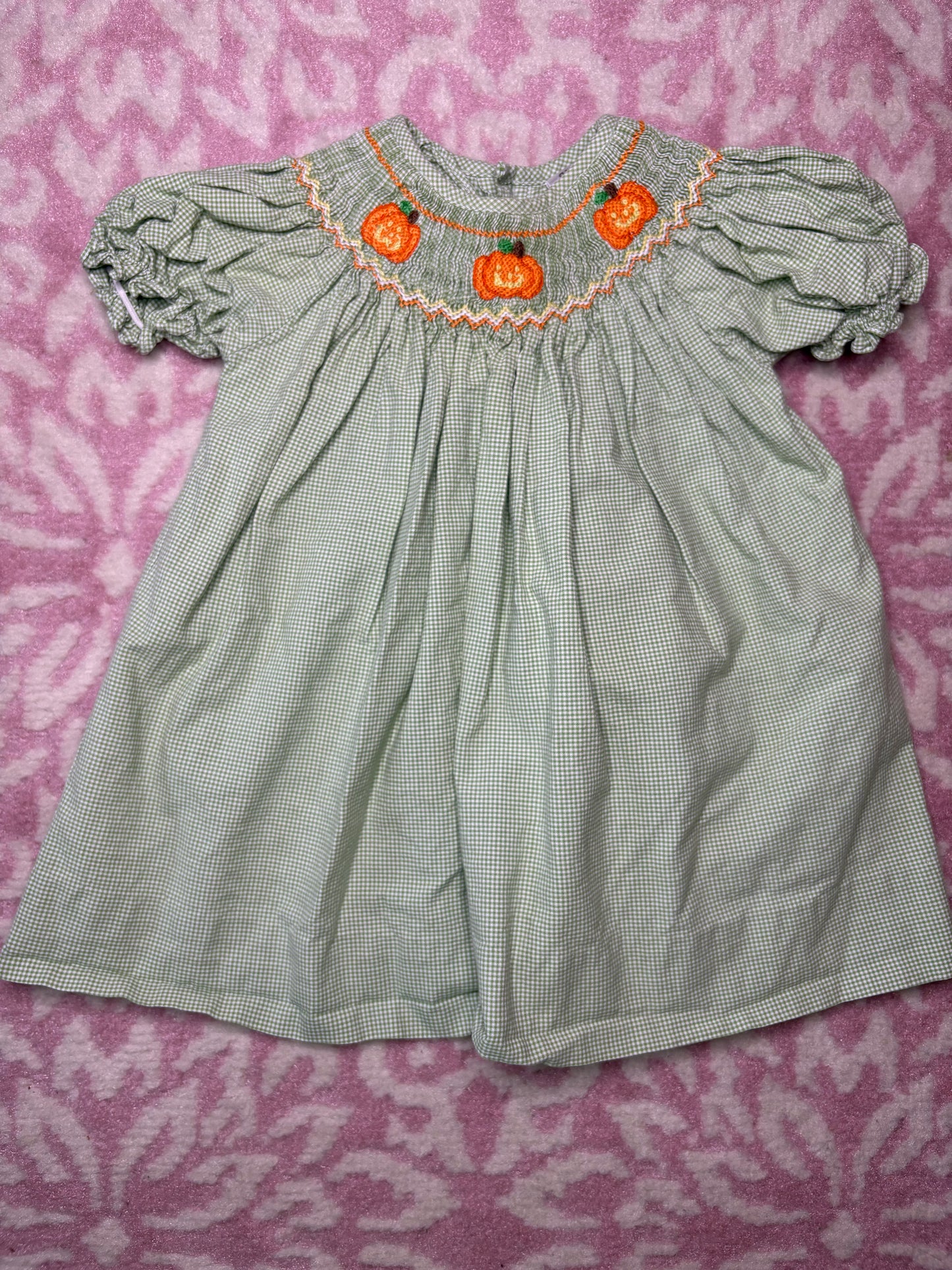 Green gingham smocked baby dress with pumpkin embroidery, short puff sleeves, on pink background