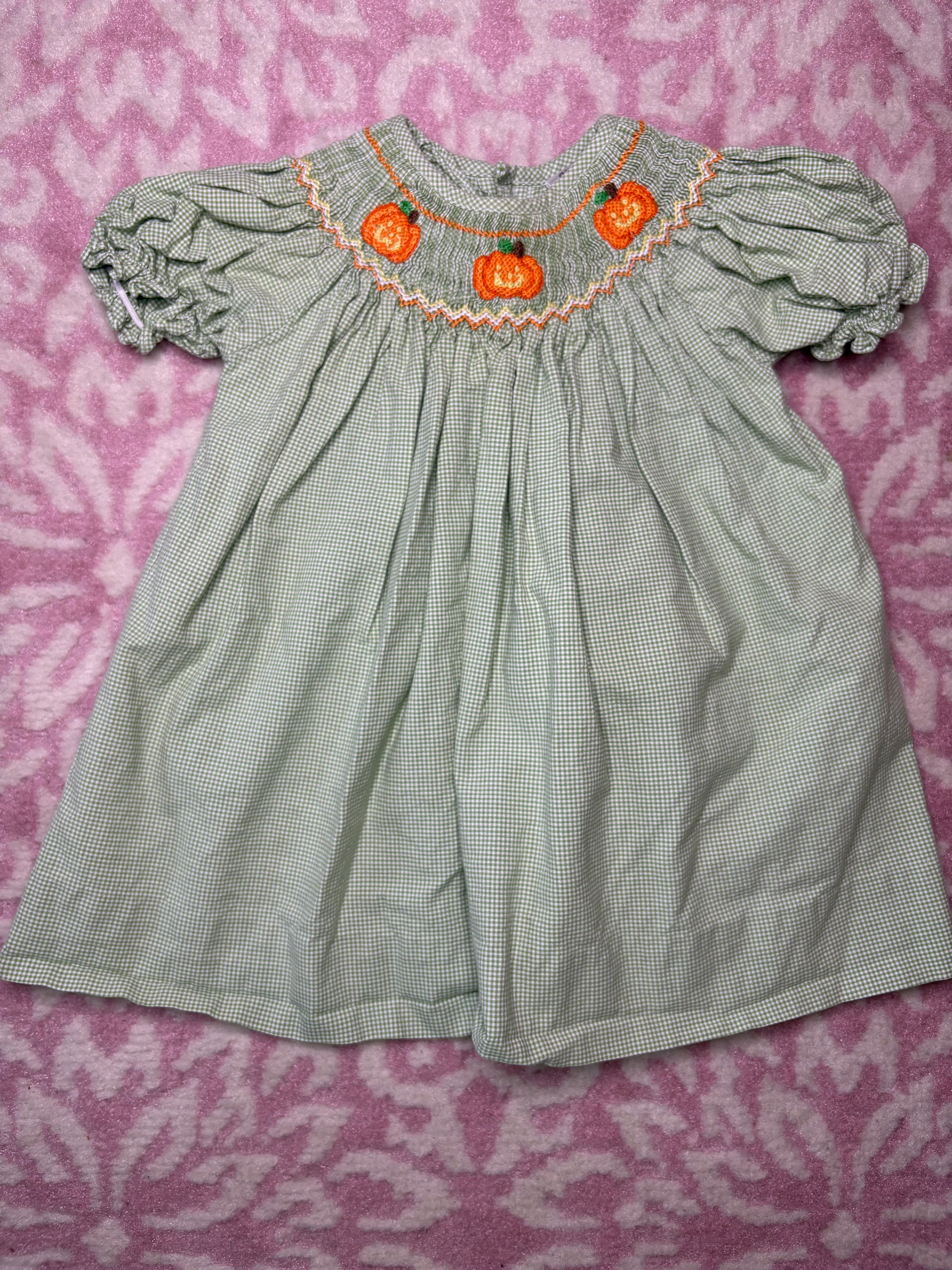 Green gingham smocked baby dress with pumpkin embroidery, short puff sleeves, on pink background