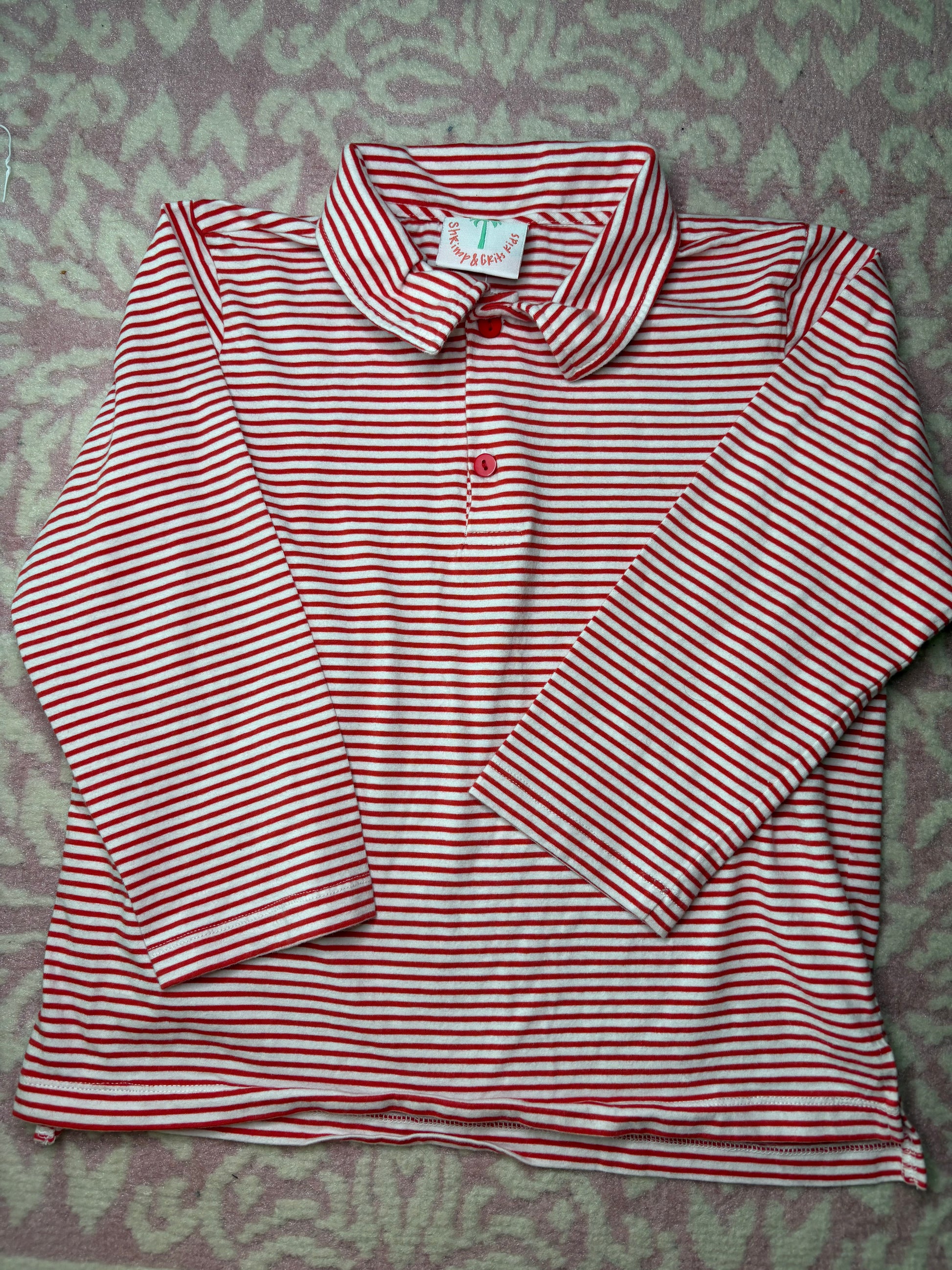 Red and white striped long sleeve children's shirt with collar, laid flat on patterned background
