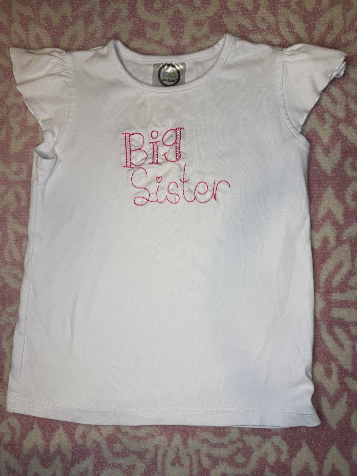 White short sleeve girls shirt with pink 'Big Sister' embroidery on patterned background