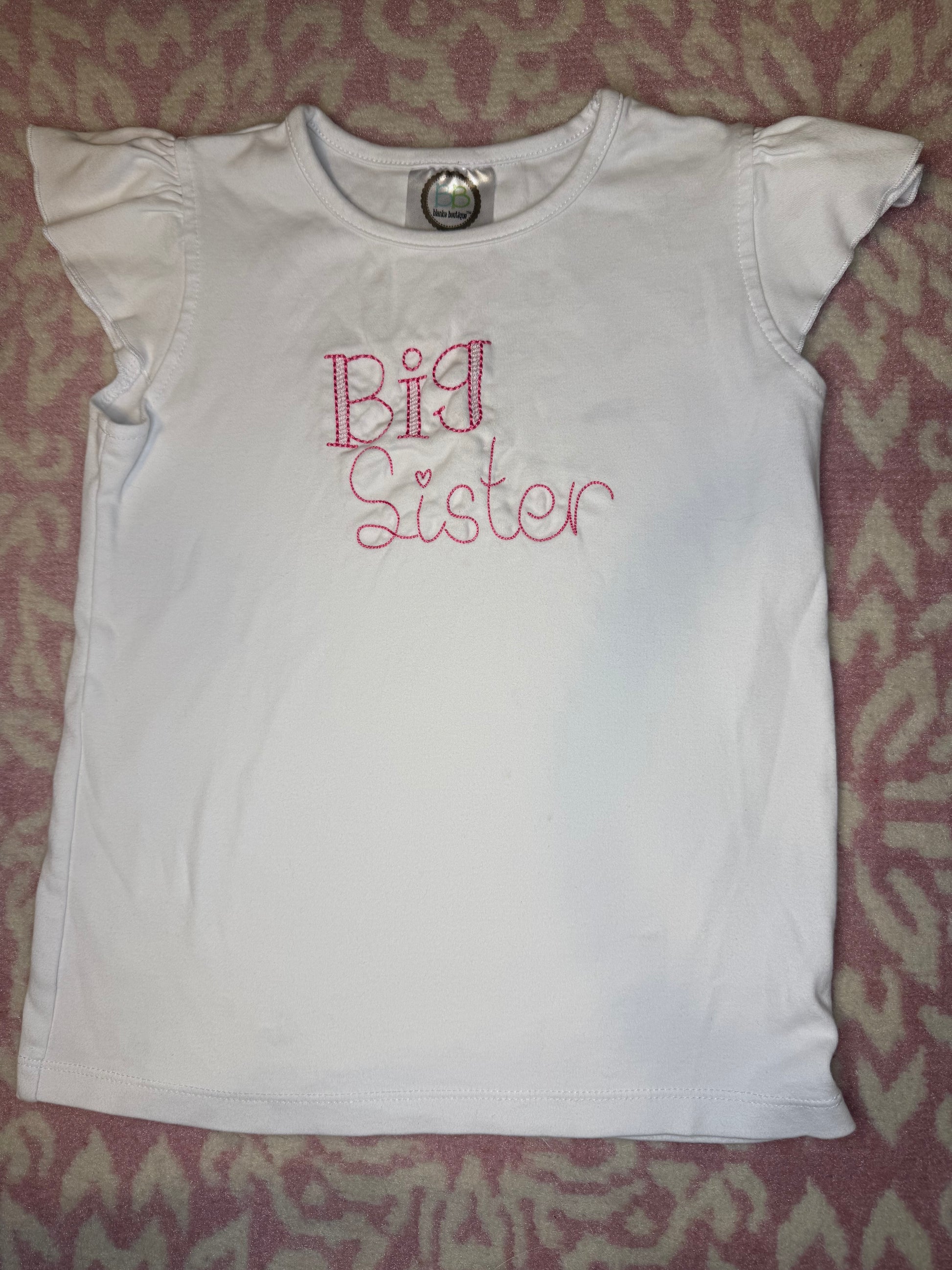 White short sleeve girls shirt with pink 'Big Sister' embroidery on patterned background