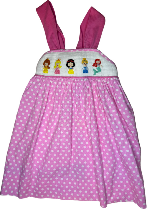 Pink polka dot dress with embroidered Disney characters on a patterned surface