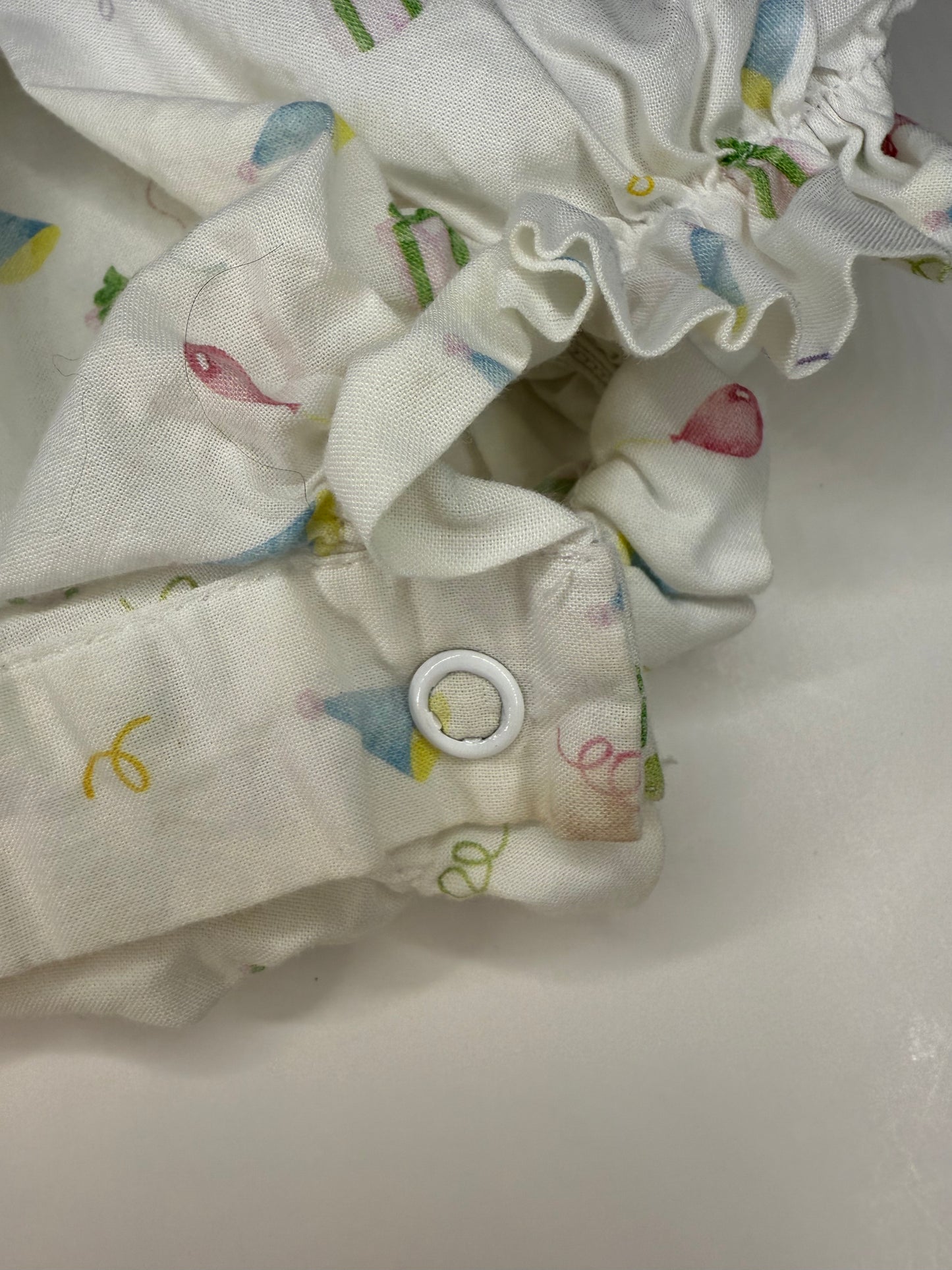 Close-up of children’s clothing fabric with colorful party hat print and snap button detail